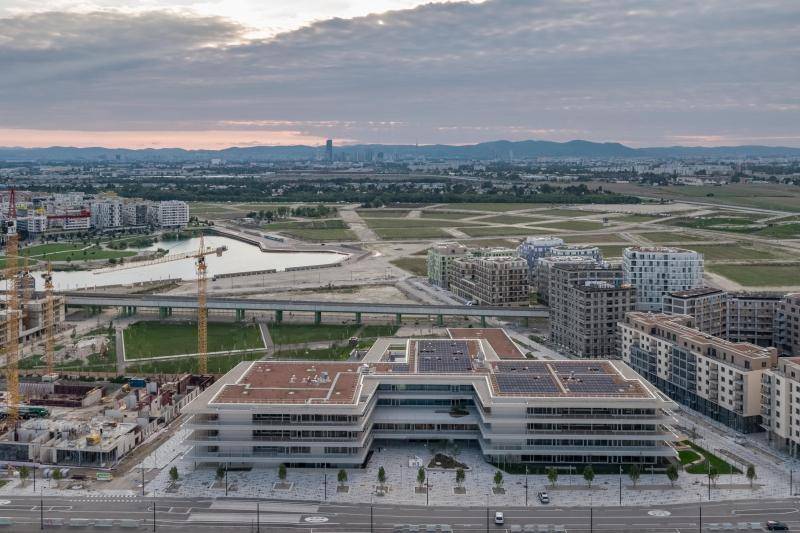 Aus der Luft ist eine Aufnahme vom gesammten Gebäude zu sehen. Die Mitte des Gebäudes ist nach hinten versetzt. Das gebäude im hellen grau ist in der Bildmitte. Auch aus der Ferne sind die vier Geschosse und die umlaufenden Balkone zu erkennen. Aus der Luft ist eine Aufnahme vom gesammten Gebäude zu sehen. Die Mitte des Gebäudes ist nach hinten versetzt. Das gebäude im hellen grau ist in der Bildmitte. Auch aus der Ferne sind die vier Geschosse und die umlaufenden Balkone zu erkennen.