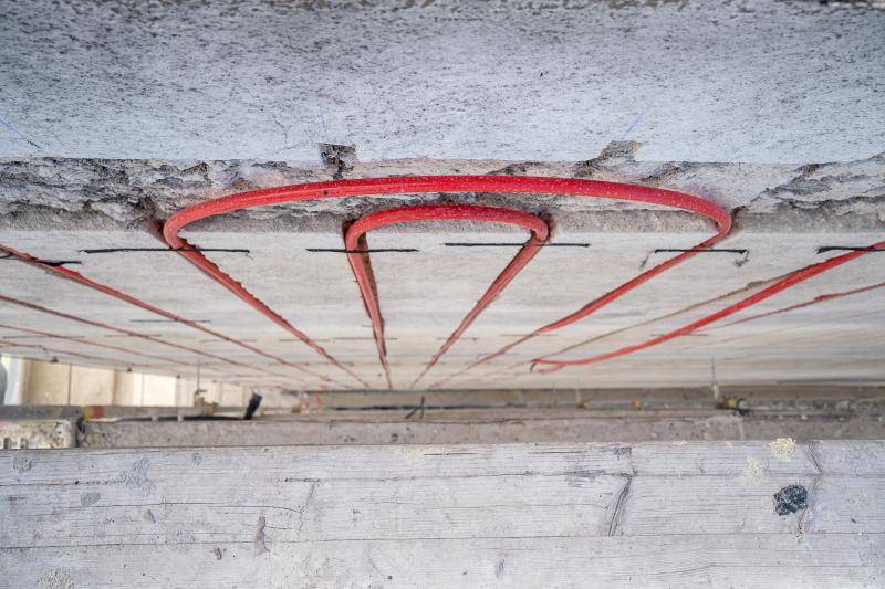 Bild von oben nach unten fotografiert zwischen Gerüst und Fassade. Zu sehen sind die eingefrästen roten Heiz-/Kühlleitungen, die ganz oben einen halb Kreis machen und wieder zurück nach unten verlaufen. Bild von oben nach unten fotografiert zwischen Gerüst und Fassade. Zu sehen sind die eingefrästen roten Heiz-/Kühlleitungen, die ganz oben einen halb Kreis machen und wieder zurück nach unten verlaufen.