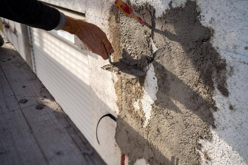 Es ist der Arm einer Person zu sehen, die in der Hand eine Kelle hält und die roten leitungen mit Spachtelmasse in der Fassade beseftigt und abdeckt. Es ist der Arm einer Person zu sehen, die in der Hand eine Kelle hält und die roten leitungen mit Spachtelmasse in der Fassade beseftigt und abdeckt.