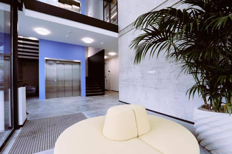 Innenaufnahmeaus dem Foyer. Sichtbetonwände, Aufzug, Treppenhaus und eine Sitzgelegenheit in gelb. Innenaufnahmeaus dem Foyer. Sichtbetonwände, Aufzug, Treppenhaus und eine Sitzgelegenheit in gelb.