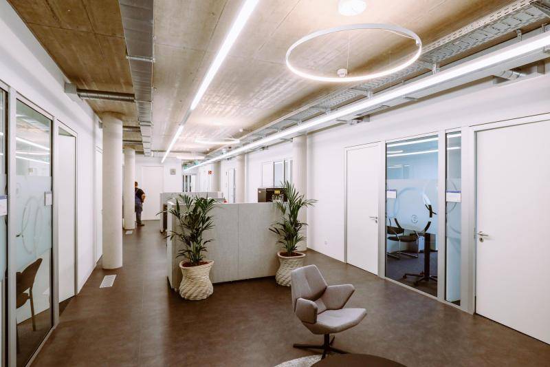 Flur zwischen Büroräumen mit Sitzmöglichkeiten und Pflanzen. Hell beleuchtet durch Lichtbänder gerade und inKreisform. Flur zwischen Büroräumen mit Sitzmöglichkeiten und Pflanzen. Hell beleuchtet durch Lichtbänder gerade und inKreisform.