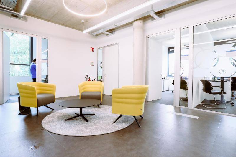 Flurbereich mit kleinem Tisch, an dem drei Sessel platziert sind. Im Hintergrund Büroräume. Flurbereich mit kleinem Tisch, an dem drei Sessel platziert sind. Im Hintergrund Büroräume.