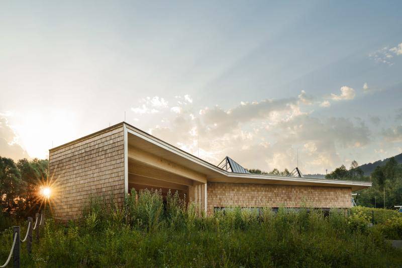 Die tiefstehende Sonne scheint durch die Bäume am Gebäudeeck vorbei. Hohe Sträucher wachsen um das Gebäude. Die tiefstehende Sonne scheint durch die Bäume am Gebäudeeck vorbei. Hohe Sträucher wachsen um das Gebäude.