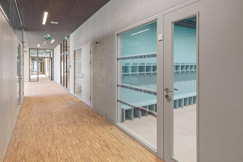 Innenansicht des Flures. Stäbchenparkett und graue Innenwände sind zu sehen. Große Glastüren gehen in die unterschiedlichen Räume ab. Die Decke ist mit Gitter-Elementen abgehängt. Innenansicht des Flures. Stäbchenparkett und graue Innenwände sind zu sehen. Große Glastüren gehen in die unterschiedlichen Räume ab. Die Decke ist mit Gitter-Elementen abgehängt.