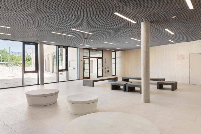 Vorbereich einer der Einrichtungen. Hier stehen vereinzelt, kleine Sitzmöglichkeiten in weiß und grau. Im Hintergrund gibt eine Glasfront den Blick nach draußen frei. Vorbereich einer der Einrichtungen. Hier stehen vereinzelt, kleine Sitzmöglichkeiten in weiß und grau. Im Hintergrund gibt eine Glasfront den Blick nach draußen frei.