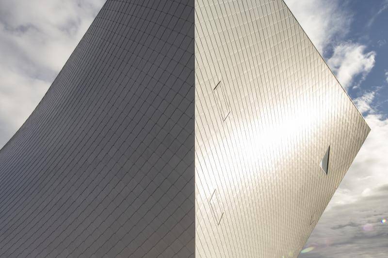 Das Gebäudeeck an dem zwei der Fassaden spitz zusammen laufen ist zu sehen. Eine der Seiten glänzt im Sonnenlicht, die Andere liegt im Schatten. Das Gebäudeeck an dem zwei der Fassaden spitz zusammen laufen ist zu sehen. Eine der Seiten glänzt im Sonnenlicht, die Andere liegt im Schatten.