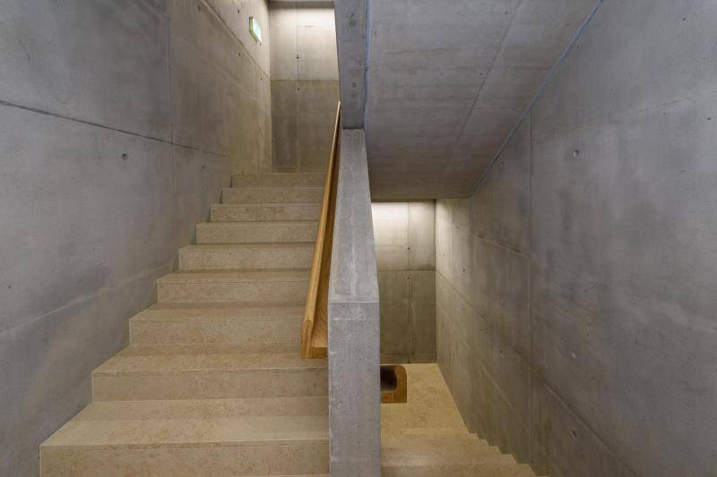 Das Treppenhaus ist aus Sichtbeton hergestellt. Die Handläufe sind Holzprofile und die Stufen selbst aus sandfarbenem Marmor. Das Treppenhaus ist aus Sichtbeton hergestellt. Die Handläufe sind Holzprofile und die Stufen selbst aus sandfarbenem Marmor.