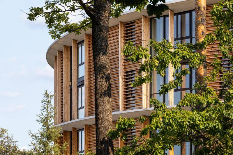 Die Holzfassade des Gebäudes ist durch einen Baum zu sehen. Die Holzfassade des Gebäudes ist durch einen Baum zu sehen.