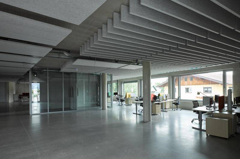 Zu sehen ist hier der Büro-Innenraum, mit Sichtestrich, Akkustikelemnenten an der Decke und Sichtbeton-Säulen im Raum. Im hintergrund sich Schreibtischen und Glaswände zu sehen. Zu sehen ist hier der Büro-Innenraum, mit Sichtestrich, Akkustikelemnenten an der Decke und Sichtbeton-Säulen im Raum. Im hintergrund sich Schreibtischen und Glaswände zu sehen.