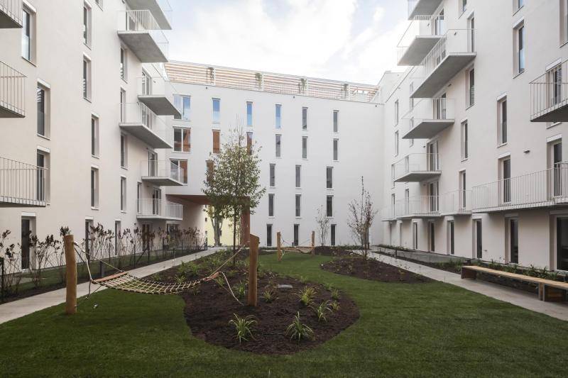 zu sehen ist eine Rasenfläche mit angelegten Beeten dazwischen, in denen kleine Streucher gepflanz sind. Die Fassaden der gebäude sind weiß. Auch die Fenster, Balkone und deren Geländer sind Alle weiß. zu sehen ist eine Rasenfläche mit angelegten Beeten dazwischen, in denen kleine Streucher gepflanz sind. Die Fassaden der gebäude sind weiß. Auch die Fenster, Balkone und deren Geländer sind Alle weiß.