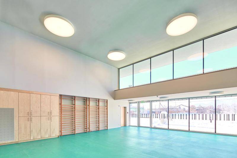 Zu sehen ist die Wand eines Sportraums. Daran angebracht sind Sprossenwände zum klettern. Recht sieht man eine zweietagige Fensterfront mit schwarzen Rahmen. An der Decke befinden sich große, runde Lichter. Der Hallenboden ist türkiser Hallenbelag. Zu sehen ist die Wand eines Sportraums. Daran angebracht sind Sprossenwände zum klettern. Recht sieht man eine zweietagige Fensterfront mit schwarzen Rahmen. An der Decke befinden sich große, runde Lichter. Der Hallenboden ist türkiser Hallenbelag.