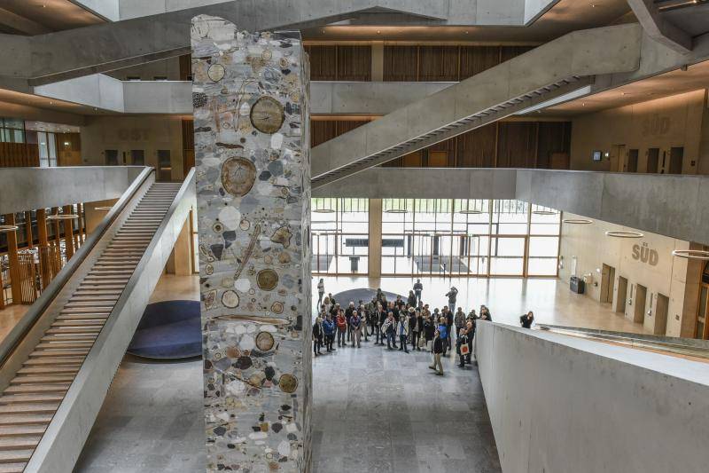 In der Mitte des großen Foyers, welches sich über die gesammte Gebäudehöhe öffnet, steht ein Betonpfeiler. Dieser ist gegossen mit Baumscheiben und großen Steinen an den Oberflächen. In der Mitte des großen Foyers, welches sich über die gesammte Gebäudehöhe öffnet, steht ein Betonpfeiler. Dieser ist gegossen mit Baumscheiben und großen Steinen an den Oberflächen.