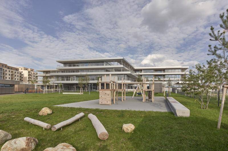 Ein Spielplatz vor dem Gebäude, umgeben von grüner Wiese und jungen Bäumen. Ein Spielplatz vor dem Gebäude, umgeben von grüner Wiese und jungen Bäumen.