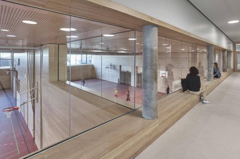 Blick durch große Glasscheiben von oben auf die Sporthallen. Diese sind mit Holz verkleidet und mit rotem Hallenboden. Blick durch große Glasscheiben von oben auf die Sporthallen. Diese sind mit Holz verkleidet und mit rotem Hallenboden.