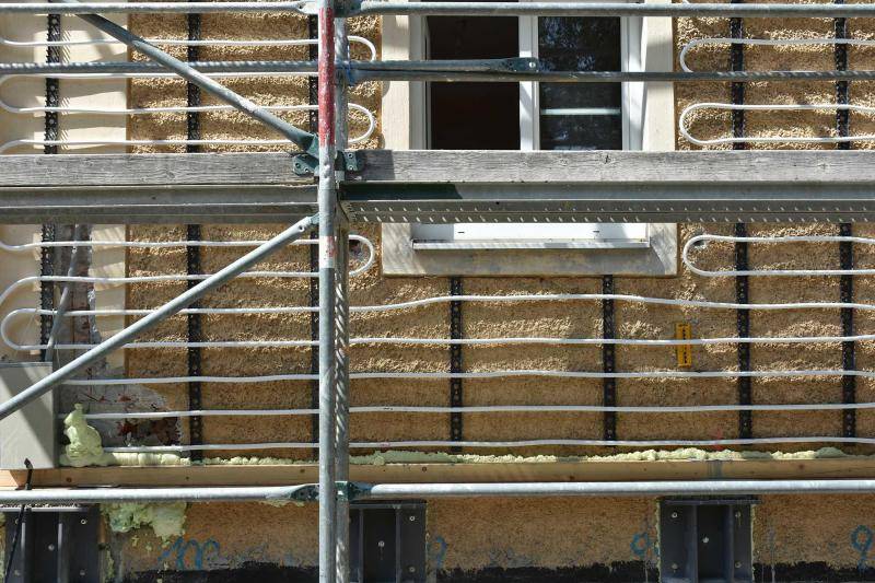 Nahaufnahme der Fassade im Bauzustand. Auf der Fassade sind weiße Schläuche zu sehen, die die Heizung der Wand werden. Sie sind in Sclangenlinien angeordnet. Nahaufnahme der Fassade im Bauzustand. Auf der Fassade sind weiße Schläuche zu sehen, die die Heizung der Wand werden. Sie sind in Sclangenlinien angeordnet.