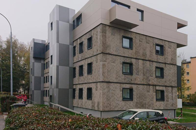 Ansicht des fertigen Gebäudes. Zu sehen das Gebäude und zwei Treppentürme, welche im Wechsel mit grauen und weißen Platten verkleidet sind. Ansicht des fertigen Gebäudes. Zu sehen das Gebäude und zwei Treppentürme, welche im Wechsel mit grauen und weißen Platten verkleidet sind.