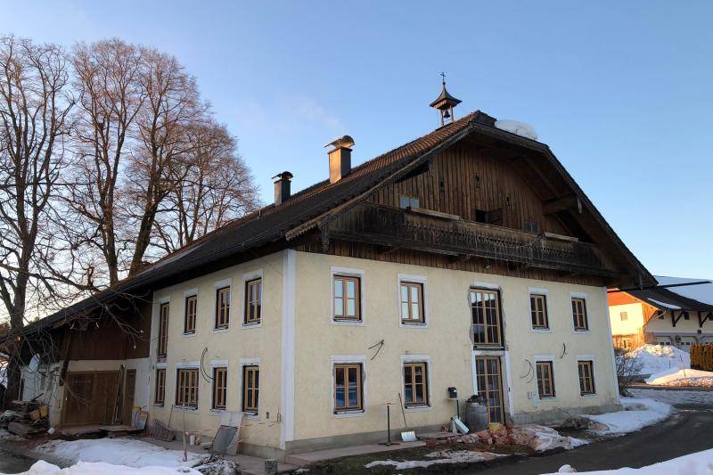 Das Bauernhaus während der Sanierung. Die unteren zwei Geschosse sind verputzt in beige. Das Dachgeschoss ist mit einer dunklen Holzschalung bekleidet. Vor dem Haus liegt Schnee. Auf dem First des Dachs ist ein kleiner Glockenturm. Das Bauernhaus während der Sanierung. Die unteren zwei Geschosse sind verputzt in beige. Das Dachgeschoss ist mit einer dunklen Holzschalung bekleidet. Vor dem Haus liegt Schnee. Auf dem First des Dachs ist ein kleiner Glockenturm.
