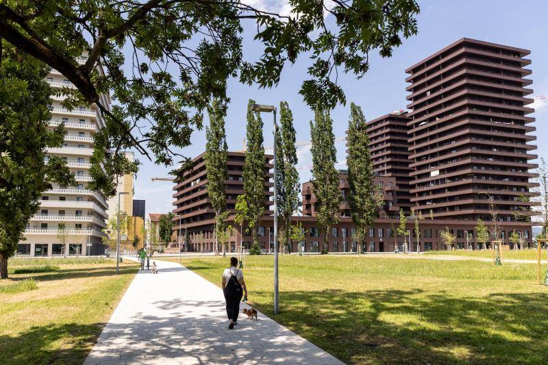 Das Gebäude bzw. die Gebäudeblocks sind im Hintergrund zu sehen. Mit seiner rot/braunen Fassaden-Farbe hebt es sich deutlich vom grünen Park mit Bäumen und Wiesen ab Das Gebäude bzw. die Gebäudeblocks sind im Hintergrund zu sehen. Mit seiner rot/braunen Fassaden-Farbe hebt es sich deutlich vom grünen Park mit Bäumen und Wiesen ab
