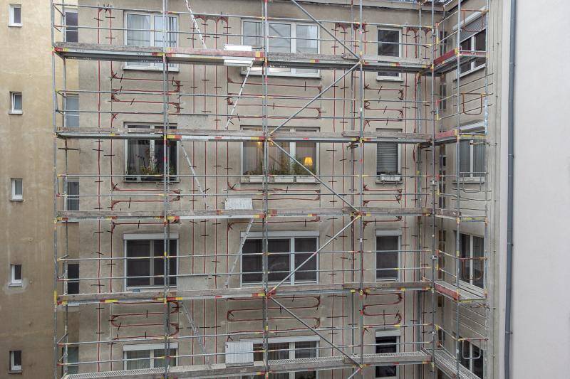 zu sehen ist ein Teil eines großen Mehrfamilienhauses, dessen Fassade mit Gerüst verbaut ist. Zwischen den Fenstern in der Fassade sind rote Leitungen zu sehen, die in die alte Fassade eingefräst und befestigt wurden. zu sehen ist ein Teil eines großen Mehrfamilienhauses, dessen Fassade mit Gerüst verbaut ist. Zwischen den Fenstern in der Fassade sind rote Leitungen zu sehen, die in die alte Fassade eingefräst und befestigt wurden.